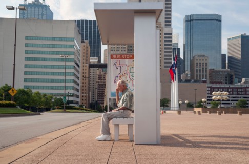 Senior man sitting at bus stop and using mobile phone