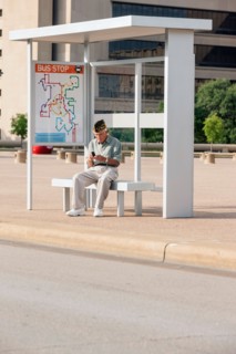 Senior man sitting at bus stop and text messaging