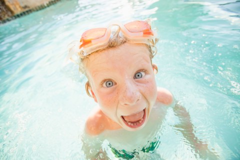 Boy (4-5) swimming in swimming pool and making funny face