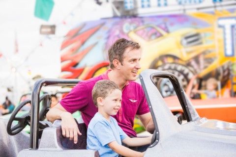 Father with son (4-5) driving toy car in amusement park
