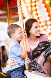 Mother and son (4-5) on carousel in amusement park