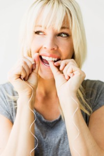 Studio portrait of blonde woman cleaning teeth with dental floss