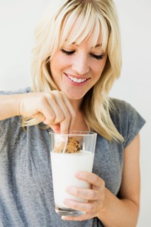 Studio portrait of blonde woman dipping cookie in milk