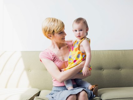 Mother with daughter (12-17 months) sitting on sofa