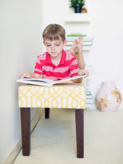 Boy (6-7) lying on bench reading book
