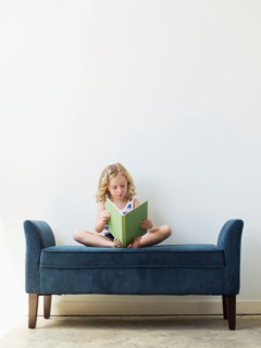 Girl (4-5) sitting on bench and reading book