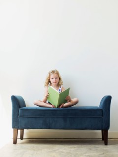 Girl (4-5) sitting on bench and reading book