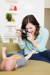 Mother sitting on sofa photographing baby boy (6-11 months)