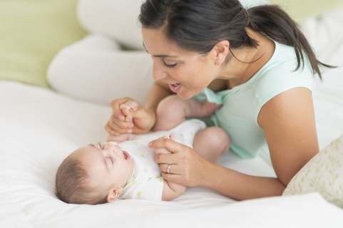 Mother and baby (2-5 months) lying on bed.