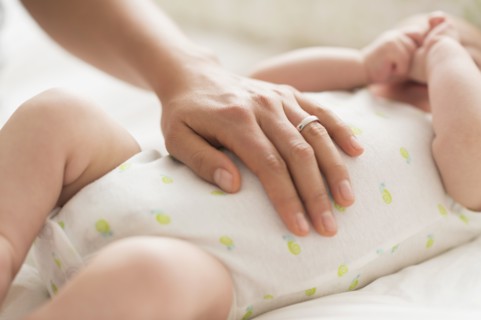 Mother massaging belly of baby boy (2-5 months).