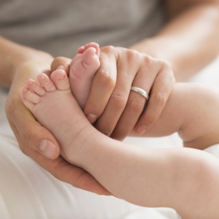 Mother holding baby boy's (2-5 months) feet.