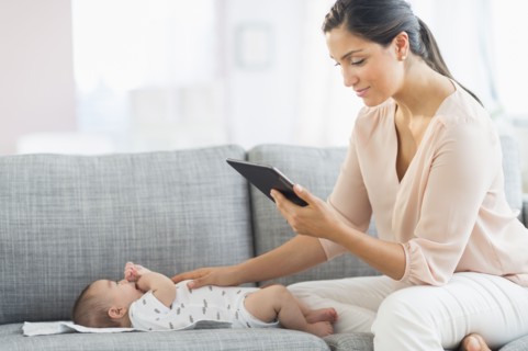 Mother playing with baby boy (2-5 months) and using digital tablet.