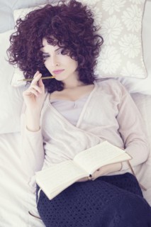 Portrait of beautiful brunette woman lying on bed with diary.