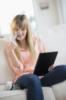 Woman sitting on sofa holding credit card and tablet pc.
Photo : Jamie Grill
