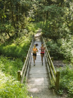Two young women running over wooden footbridge. USA, Oregon, Portland.