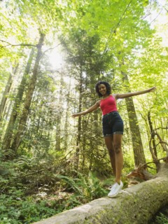 Young woman walking on log in forest. USA, Oregon, Portland.