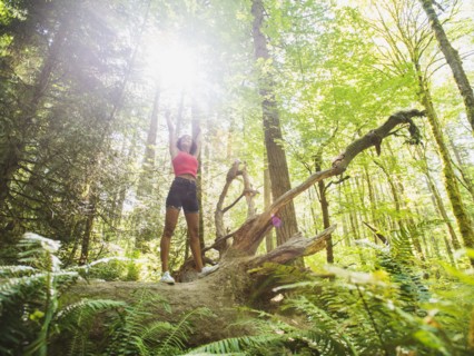 Young woman standing on log in forest. USA, Oregon, Portland.