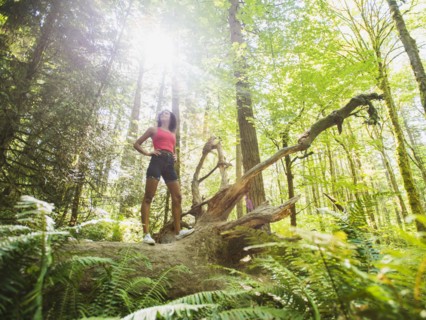 Young woman standing on log in forest. USA, Oregon, Portland.
