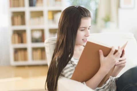 Girl (8-9) reading book in armchair.