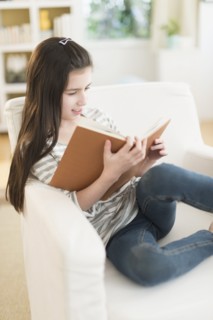 Girl (8-9) reading book in armchair.
