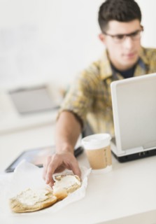 Young man eating sandwich and using laptop.