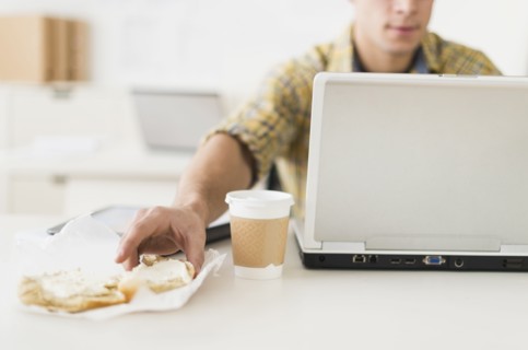Young man eating sandwich and using laptop.