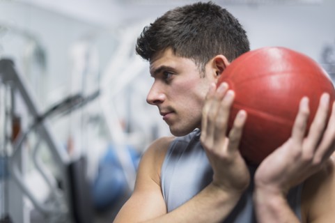 Young man at gym holding medicine ball.