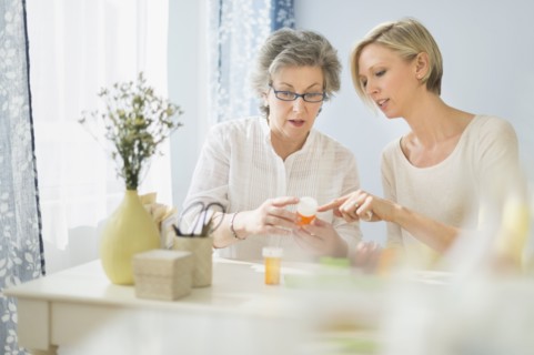 Nurse and mature woman reading labels on medicine bottle.
