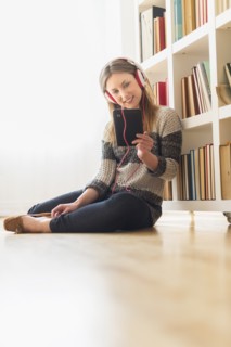 Young woman sitting on floor and listening to music on digital tablet.