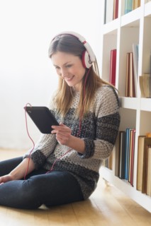 Young woman sitting on floor and listening to music on digital tablet.