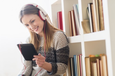 Young woman sitting on floor and listening to music on digital tablet.