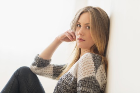 Portrait of attractive young woman sitting by wall.