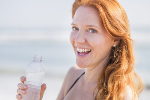 Portrait of woman drinking water on beach.