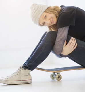 Portrait of young woman sitting on skateboard.