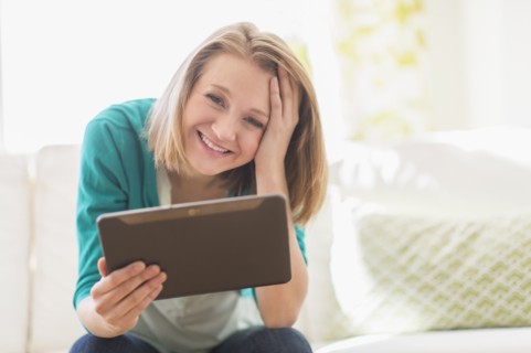 Portrait of woman on sofa holding digital tablet.
