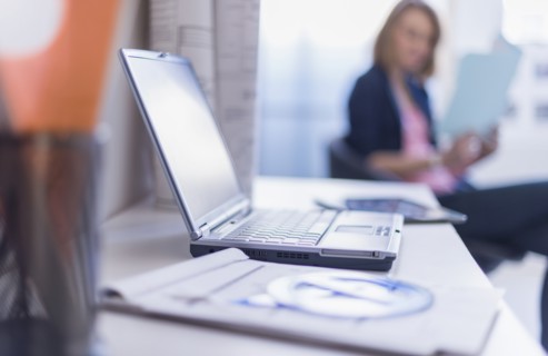 Close up of laptop and digital tablet on desk, woman in background.