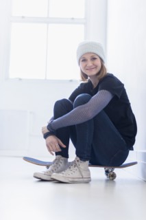Portrait of young woman sitting on skateboard.