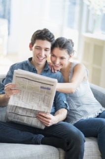 Couple reading newspaper on sofa.