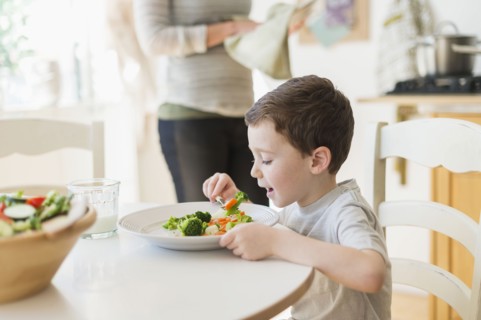 boy (6-7) eating healthy dinner, mother in background.