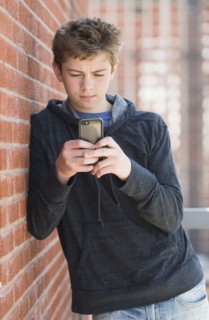 Teenage boy (16-17) leaning against brick wall texting.