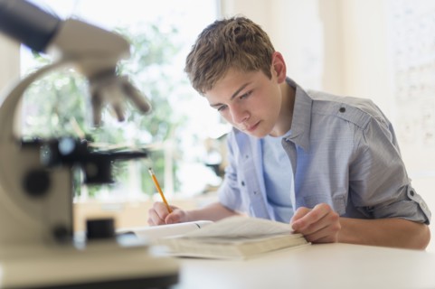 Teenage boy (16-17) reading book in laboratory.