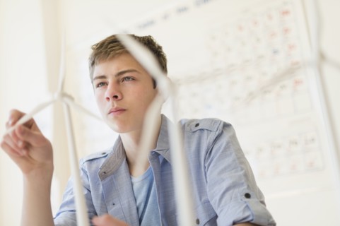Teenage boy (16-17) touching wind turbines models.