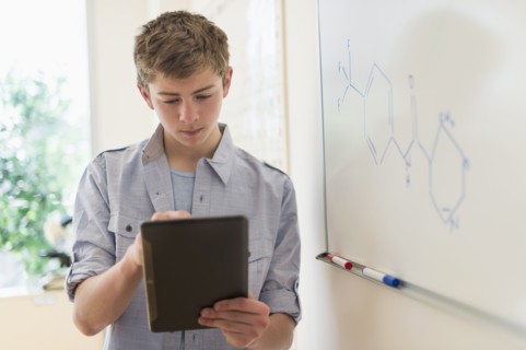 Teenage boy (16-17) using digital tablet in classroom.