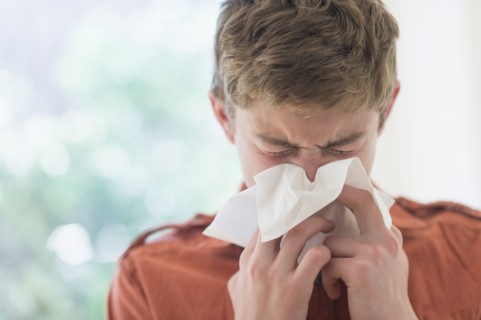 Teenage boy (16-17) blowing nose.
