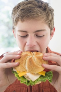 Teenage boy (16-17) eating cheese and turkey sandwich.