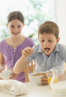 Boy and girl (8-9, 10-11) eating cereals.