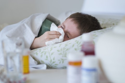 boy (8-9) lying in bed and blowing nose.