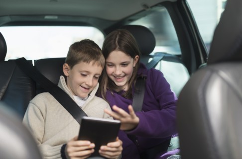 Boy and girl (8-9, 10-11) using digital tablet in car.