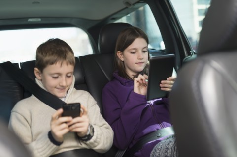 Boy and girl (8-9, 10-11) using digital tablet and smart phone in car.