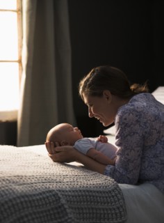 Mother holding baby boy (2-5 months) in bedroom.